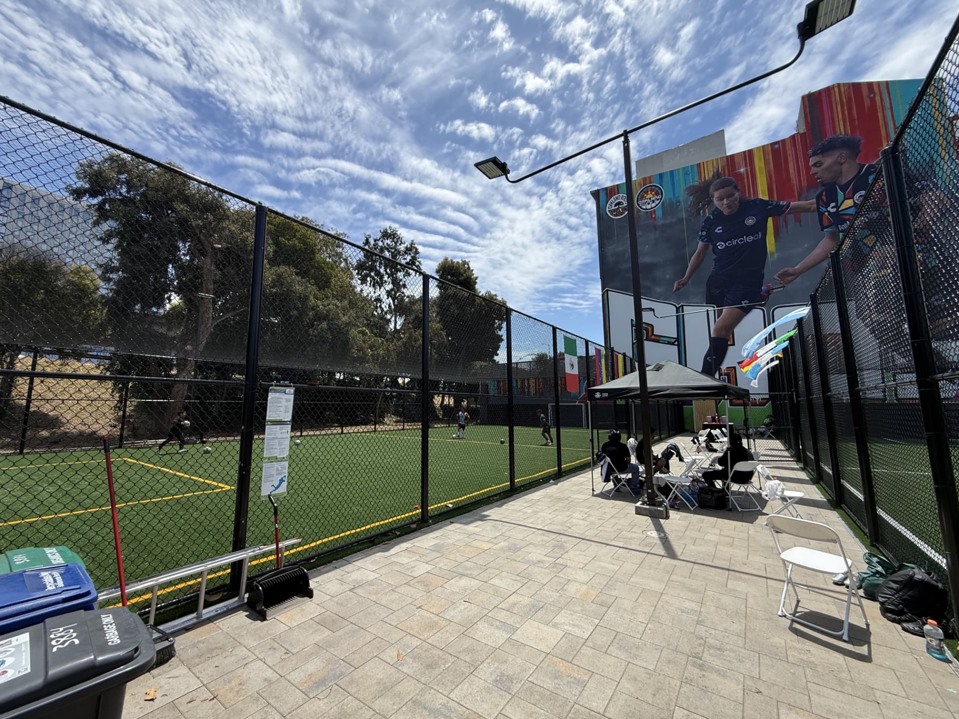 Sideline patio at Longfellow Fields with shade tent, chairs and players training on the turf